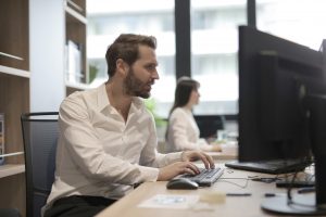 thoughtful-young-bearded-manager-typing-on-keyboard-while-3966786